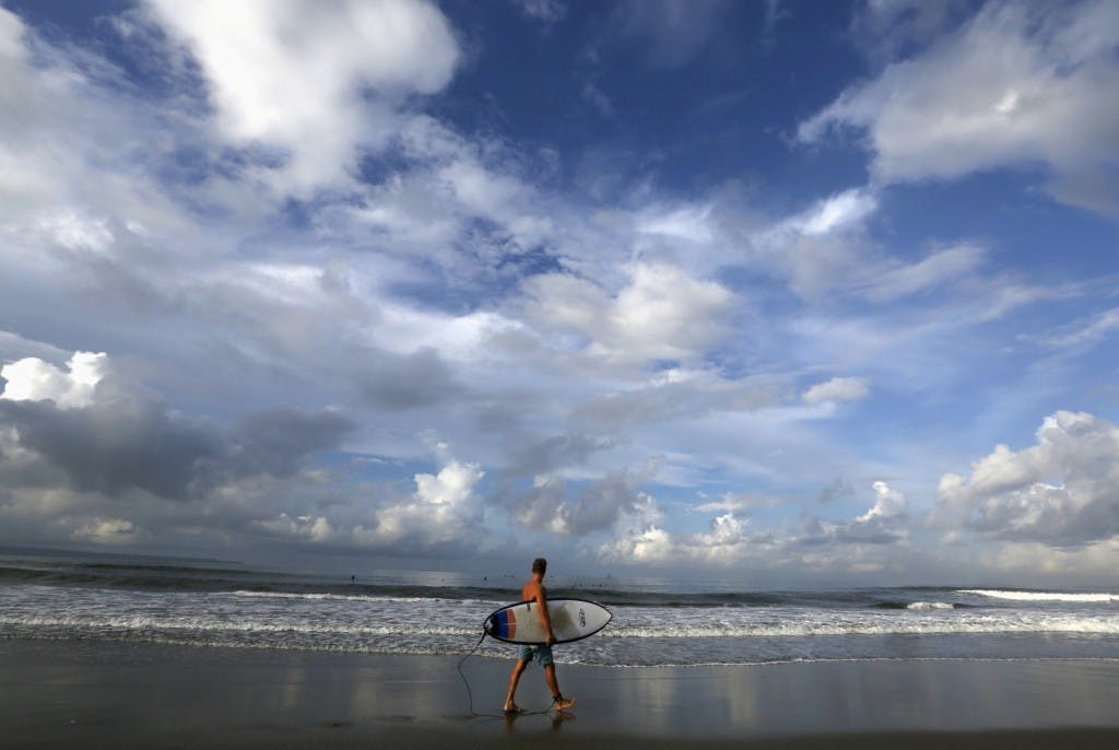 A tourist holds a surfboard as he walks in Kuta beach on the resort island of Bali