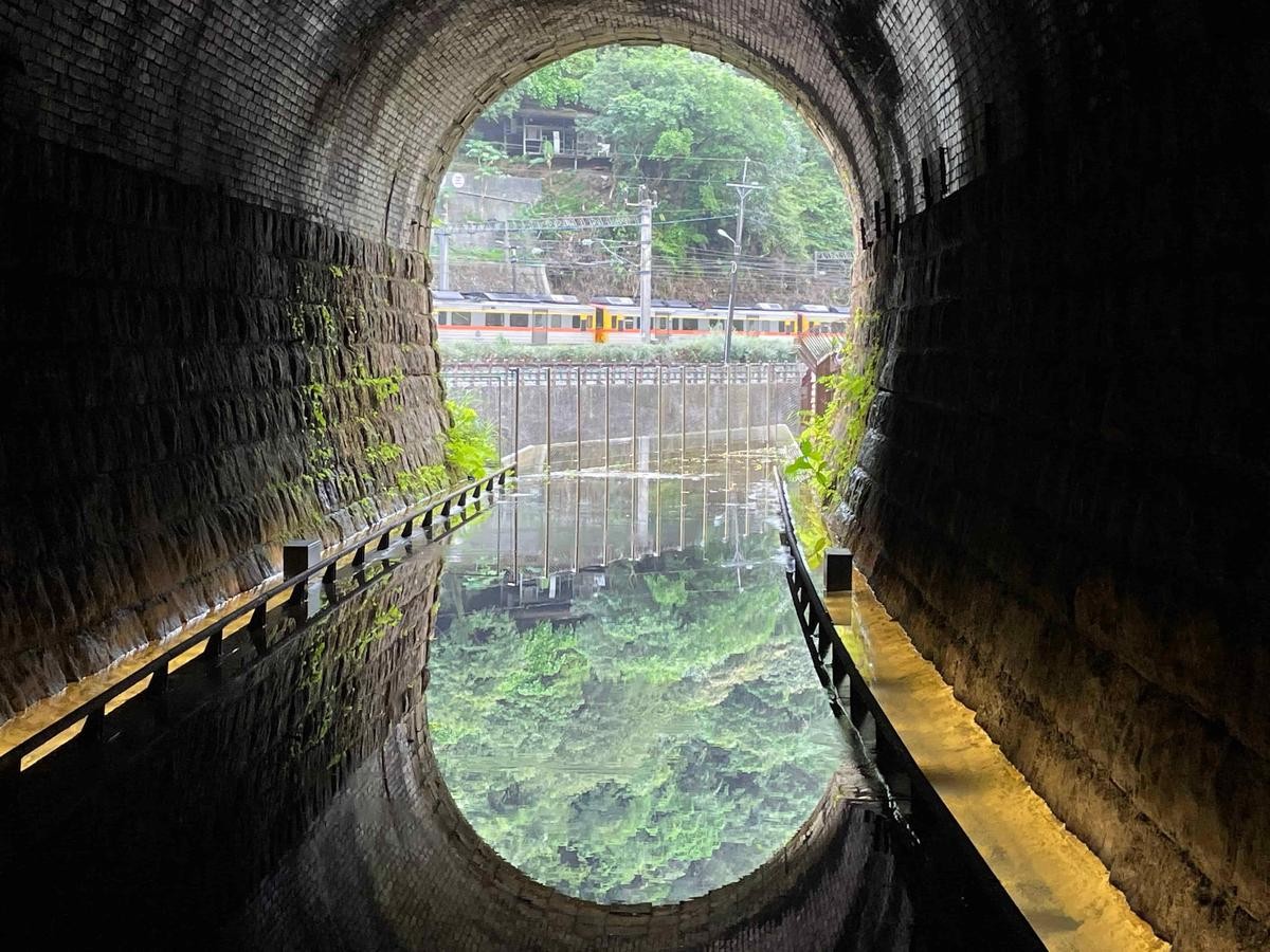 在三爪子隧道設計的鏡面水池反射出翠綠山色及火車行經影像。（新北市觀旅局提供）