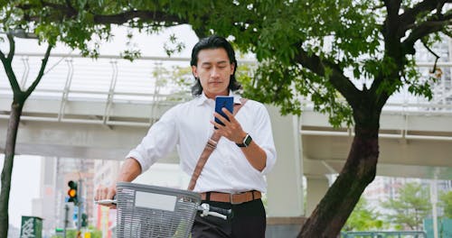 Asian,Man,Using,Phone,Walking,With,A,Sharing,Bike,Commuting