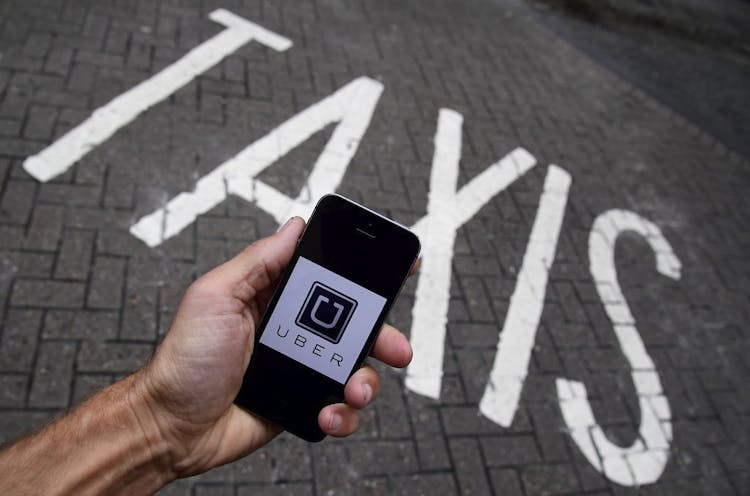 A photo illustration shows the Uber app logo displayed on a mobile telephone, as it is held up for a posed photograph in central London